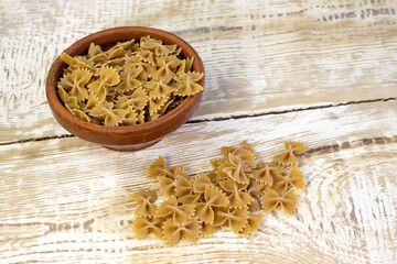 Whole grain dark pasta bows on brown plate on a rough wooden light background with selected focus