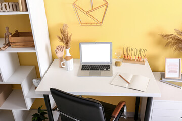 Modern laptop, cup, notebook and stylish decor on table near color wall
