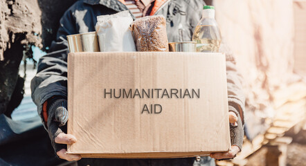 Concept banner humanitarian aid to refugees. Old man senior is holding cardboard box of donations canned food, looking camera