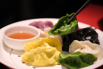 close up chopsticks pick up colorful Chinese dumplings in plate. Dumplings with stuffing and color
