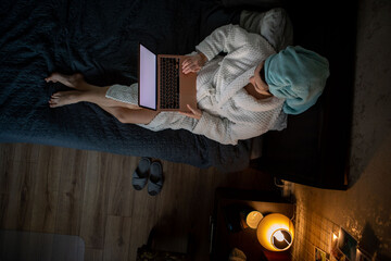 woman working on laptop at home laying in bed wet head covered with towel