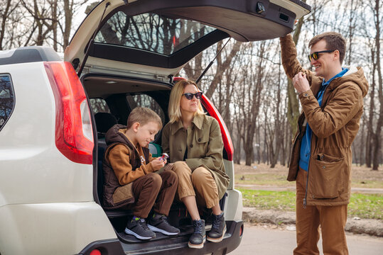 Young Family Packing For Car Travel. Putting Bags Into Trunk