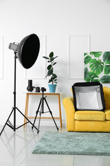 Comfortable sofa, table and modern equipment near light wall in stylish photo studio interior