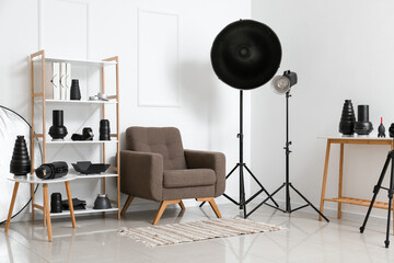 Fototapeta na wymiar Interior of light photo studio with armchair, shelf unit and different modern equipment