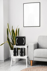 Modern loudspeakers on stepladder stool near sofa in living room interior