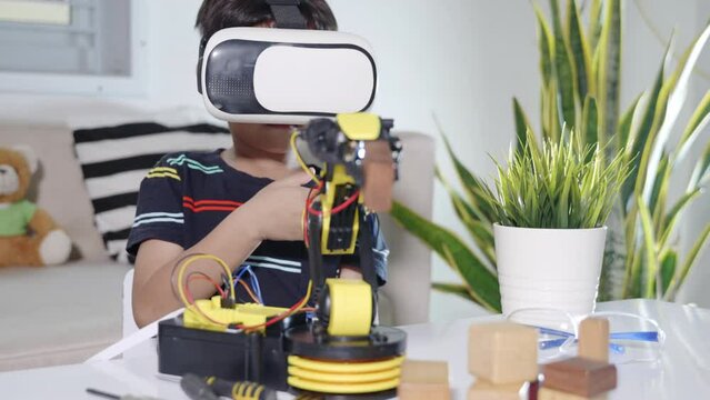 Virtual Reality Simulator. Asian kid boy using VR glasses on robotic arm in workshop, Child learning programer control robot arm with sensors to pick up wood block, Technology education. industry 4.0