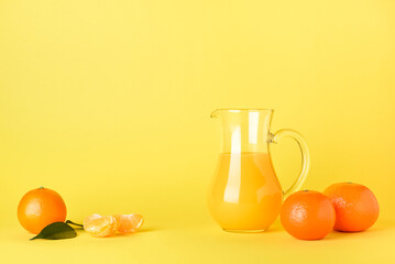 Jug of fresh tangerine juice on yellow background