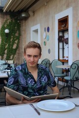 Młody mężczyzna siedzący w restauracji, trzymający menu oraz patrzący w obiektyw
