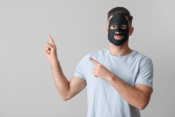 Handsome man with black facial mask pointing at something on grey background