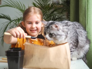 Little toddler girl planting seeds in the pots with cat. Love of pets. Funny and curious pets. Home gardening, transplanting plants, seedlings