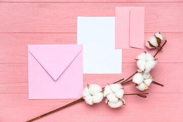 Envelopes with blank card and cotton flowers on pink wooden background