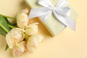 Beautiful flowers with gift box on beige background, closeup