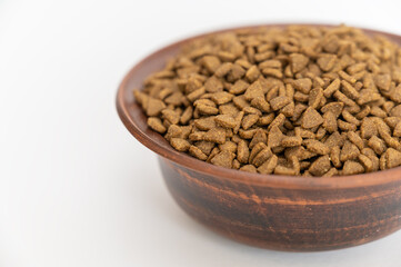Pet food. Dry pelleted food in a brown clay bowl against a white background. The pellets are triangular.