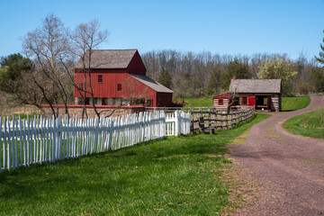 Dirt road with picket fence and a colonial American red barn and log cabin