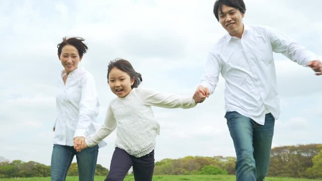 手を繋いで草原を走る親子　ファミリー　子育て　自然環境