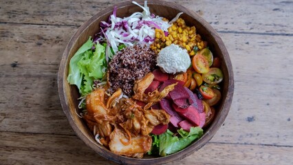 Put on the wooden table a vegetarian light salad of various types of vegetables in a wooden rounded dish. Salad is sure to appeal to adherents of vegetarian food. Saturated tasty bowl.