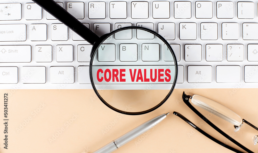 Poster text core values on keyboard with magnifier , glasses and pen on beige background