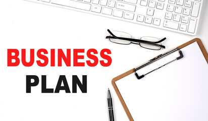 BUSINESS PLAN text written on the white background with keyboard, paper sheet and pen