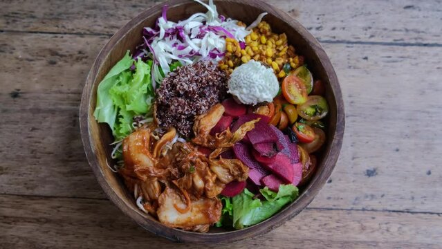 Put on the wooden table a vegetarian light salad of various types of vegetables in a wooden rounded dish. Salad is sure to appeal to adherents of vegetarian food. Saturated tasty bowl.