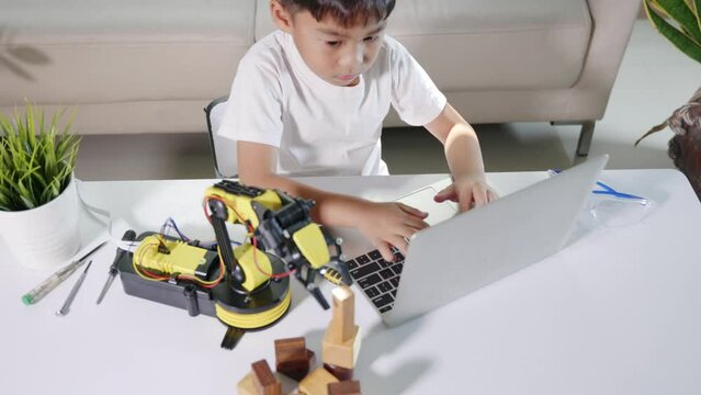 Asian little kid boy using laptop computer check on robotic arm machine in workshop, Child learning lesson programer to programming control robot arm pick up wood block, Technology science education
