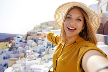Beautiful young woman taking self portrait showing Oia famous village in Santorini Island, Greece