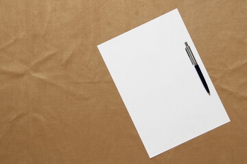 Template of white paper with pen lies diagonally on light brown cloth background. Concept of business plan and strategy. Stock photo with empty space for text and design.