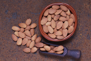 Natural almonds in brown ceramic bowl and black wooden spoon on brown tin can background