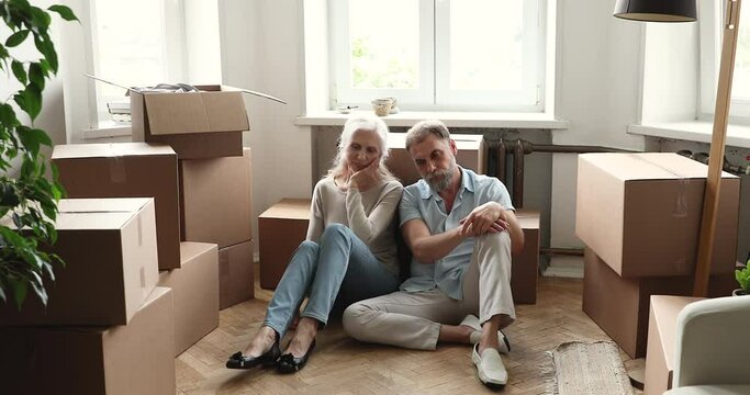 Exhausted aged couple take break in unboxing belongings at relocation day sit on floor at new flat rest of too difficult job lost in sad thoughts. Older spouses tired of doing renovation work at home