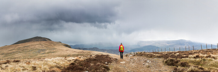 Active senior woman with backpack hiking on mountain under cloudy sky