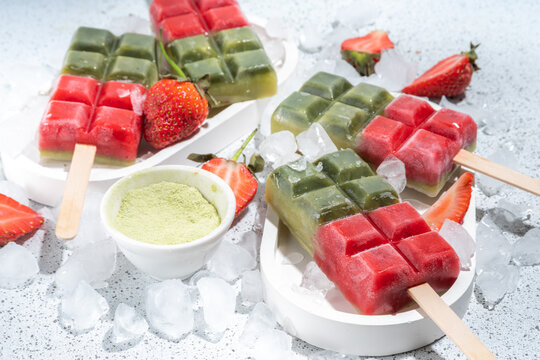 Dairy free green matcha and strawbery popsicles. Vegan ice cream popsicles with green matcha tea powder and dresh strawberry juice, Summer healthy organic dessert on white concrete background