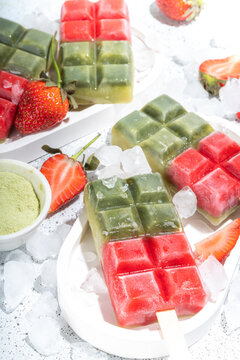 Dairy free green matcha and strawbery popsicles. Vegan ice cream popsicles with green matcha tea powder and dresh strawberry juice, Summer healthy organic dessert on white concrete background