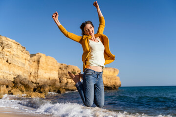 Excited woman jumping in front of sea at beach