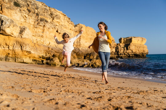 Happy mother with daughter running on shore at beach