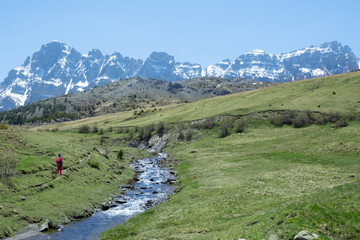 Fototapeta na wymiar Hiker in the Escarra river with snowy mountains in the background, Huesca Pyrenees.