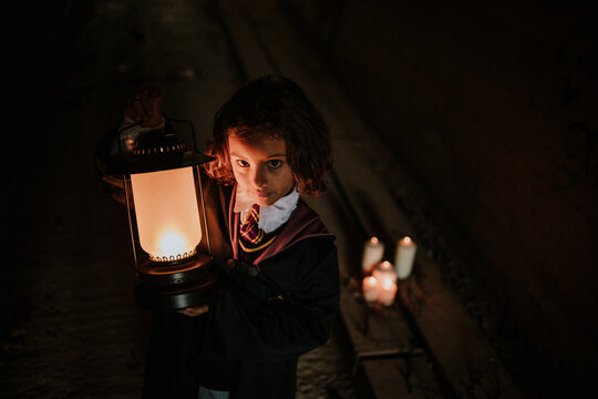 Girl with lantern wearing witch costume standing in spooky dark tunnel