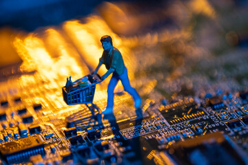 Computer mother board and figurine of man pushing shopping cart symbolizing online shopping