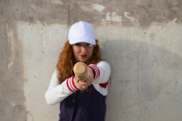 Obraz na płótnie Canvas young and beautiful red-haired woman with baseball cap, jacket with baseball bat defying camera. she is on grey concrete background. Sport and recreation concept