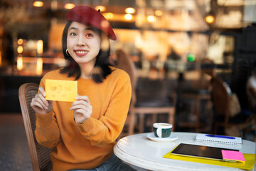 Beautiful young chinese girl in cafe. Happy girl in cafe holding sticky notes with hearts.