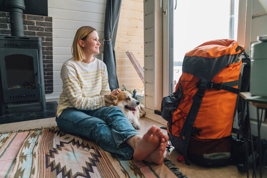Woman sitting by backpack stroking dog at home