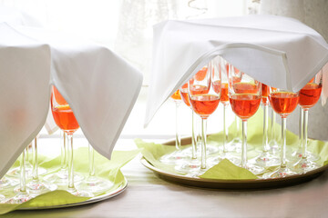 Orange aperol cocktails in champagne glasses covered with white napkins on green trays, prepared as...