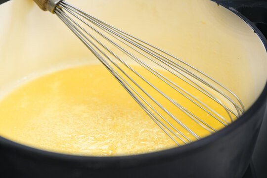 Wire whisk in a pot with golden yellow semolina flummery or pudding, cooking a delicious dessert, copy space, selected focus