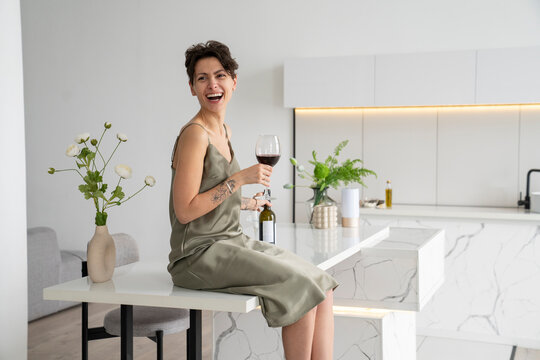 Happy woman holding wineglass sitting on kitchen island at home