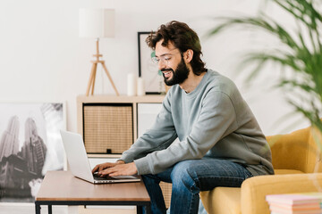 Smiling man wearing eyeglasses using laptop at home