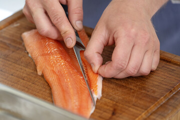 Hands of a cook remove the belly flap with bones of a fresh raw char fish with a filleting knife on...