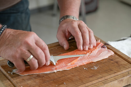 Char fish preparation, cook is removing the bones with a thin filleting knife on a cutting board in a restaurant kitchen, selected focus