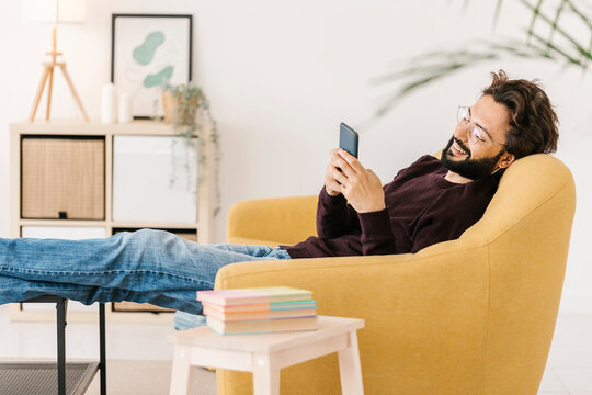Relaxed man using smart phone sitting on sofa at home