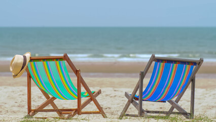 Colorful beach chairs with hat on the beach and sea waves and blue sky in the background.