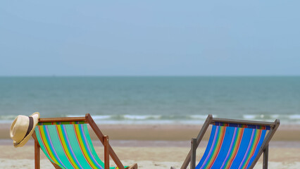 Colorful beach chair with hat on the beach and sea waves and blue sky in the background.