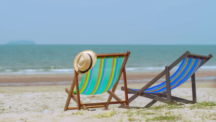 Colorful beach chairs with hat on the beach and sea waves and blue sky in the background.