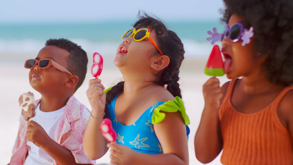 Group of children eating ice cream while having a picnic on the beach during summer vacation.